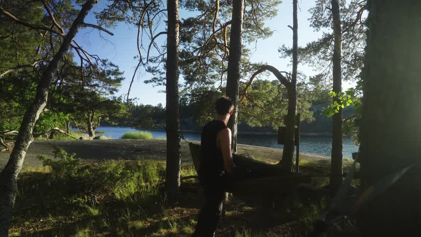 A man packs a hammock in the forest next to a river