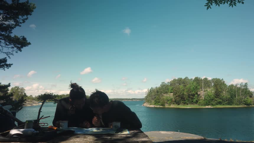 Two men looking at a map while sitting near the coast across from a forested island