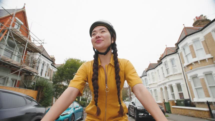 A woman in a yellow jacket and helmet riding a bicycle on a residential street