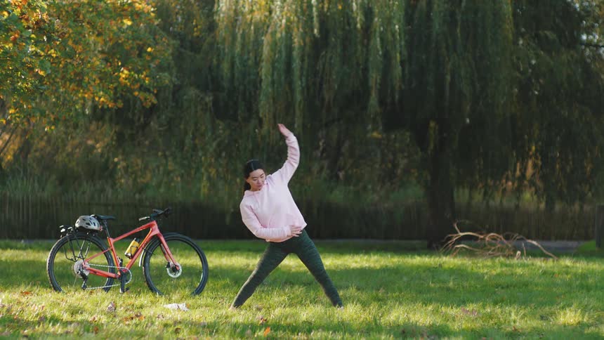A woman in a park next to a bicycle doing stretching exercises