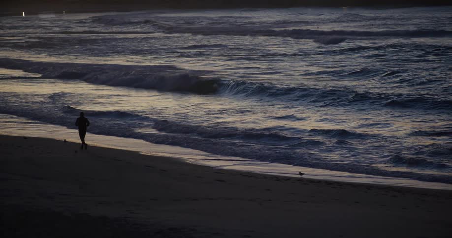 A lone figure runs along a beach at twilight