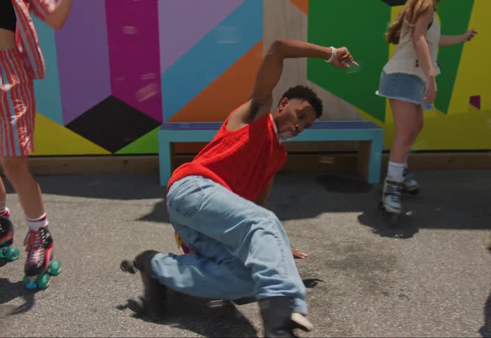 A man in an orange shirt is doing a dance where he is moving his legs and he is leaning on the ground with his arm