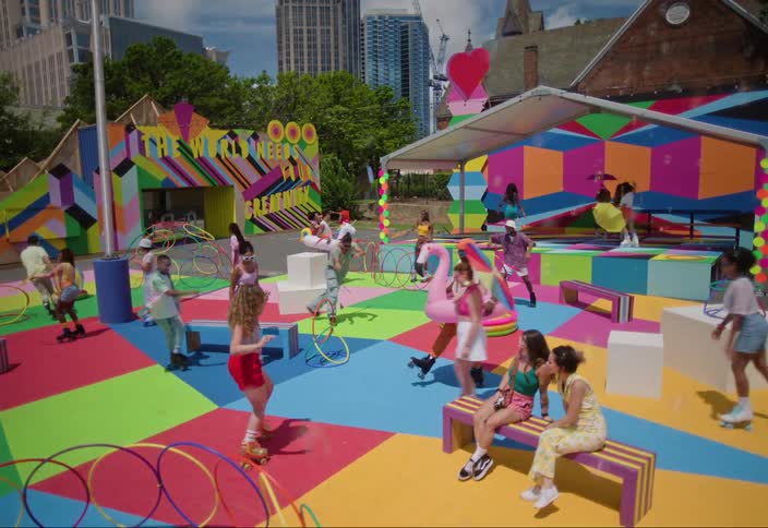 A crowd of people roller skates and dances in a colorful park