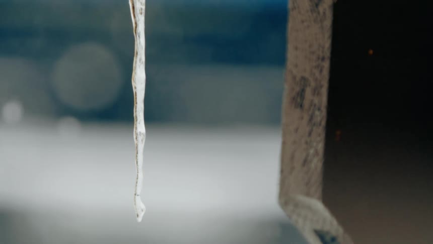 An icicle hangs near a wooden structure out of focus snow falling behind