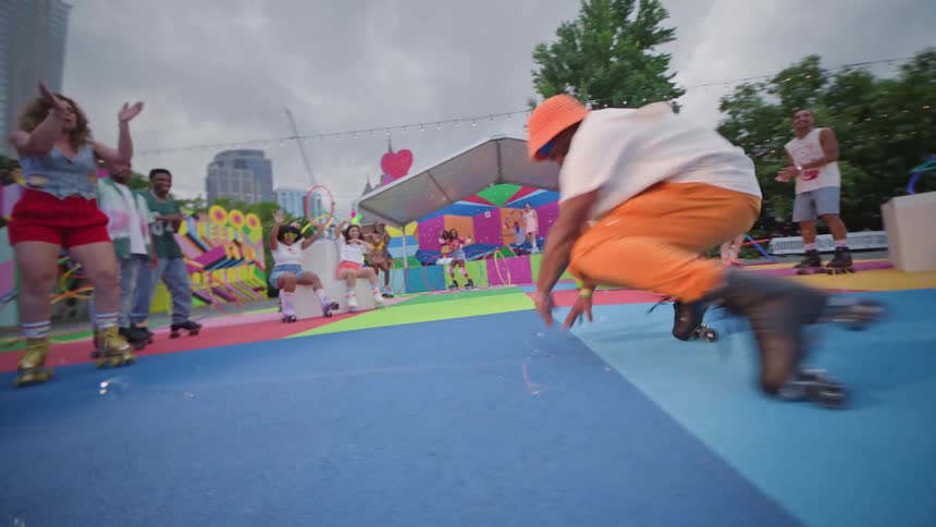A person in orange pants and black roller skates performs a dance at a vibrant skate park