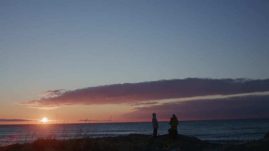 A serene sunset at the beach with two silhouetted figures standing against the sky