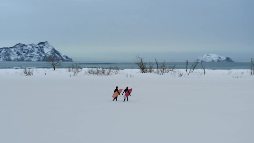 Two surfers walking in a region with the ground covered in snow