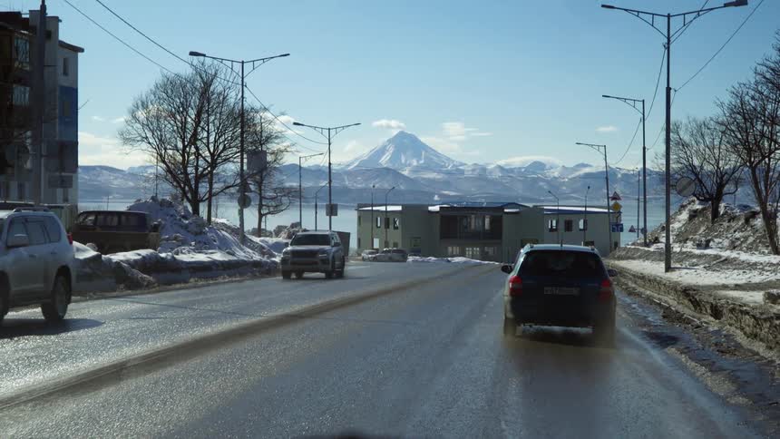 A street view with vehicles a clear sky and a prominent snowcapped mountain in the background