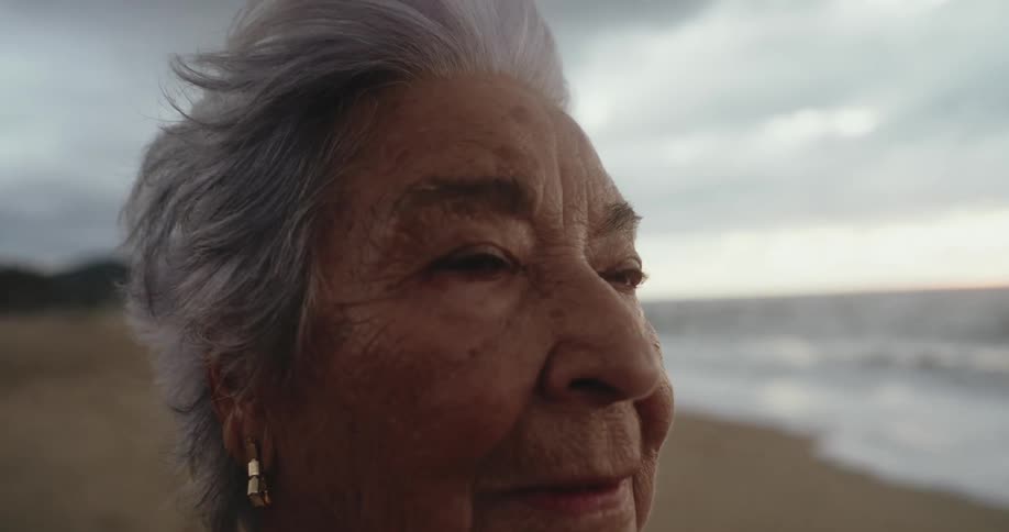 Elderly woman standing on the beach on a cloudy day looks around