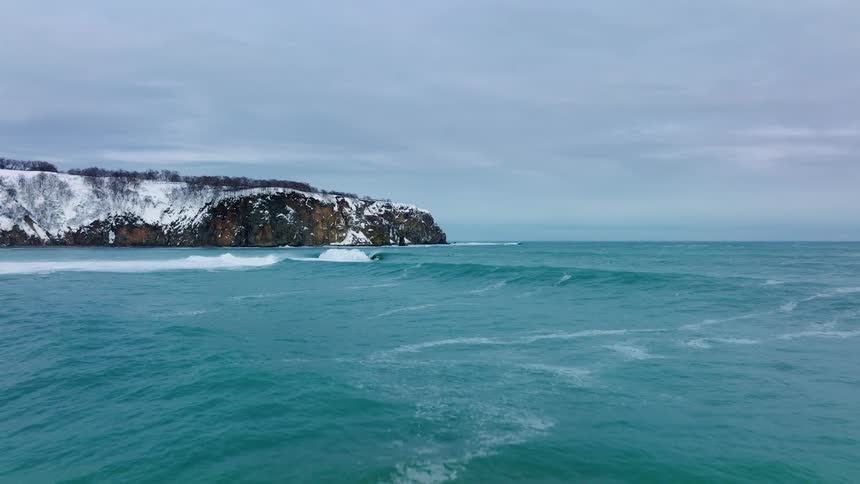Aerial panorama of a turquoise blue sea with rocky coast on the horizon with snow