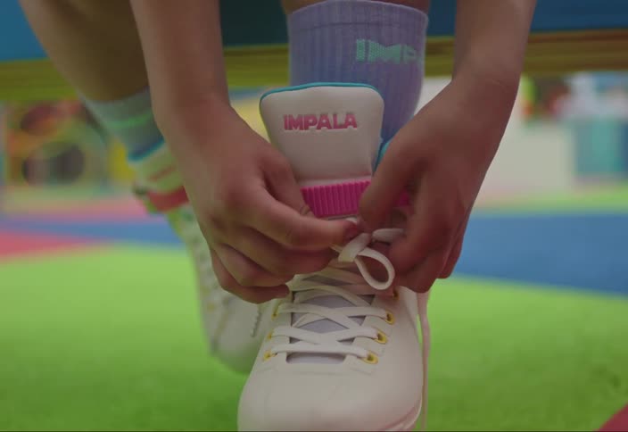 A persons hands tie the laces of a white roller skate with blue wheels