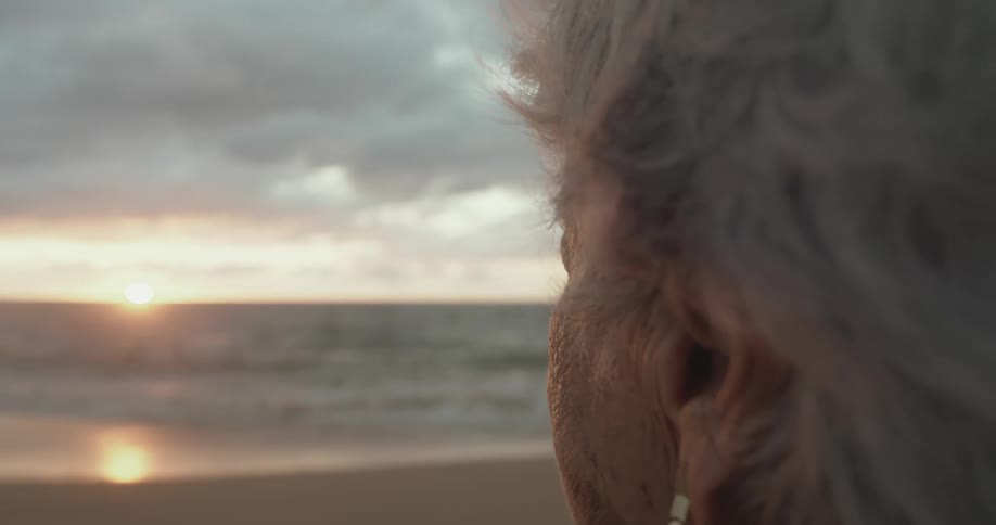An elderly woman looks into the sunset from the beach