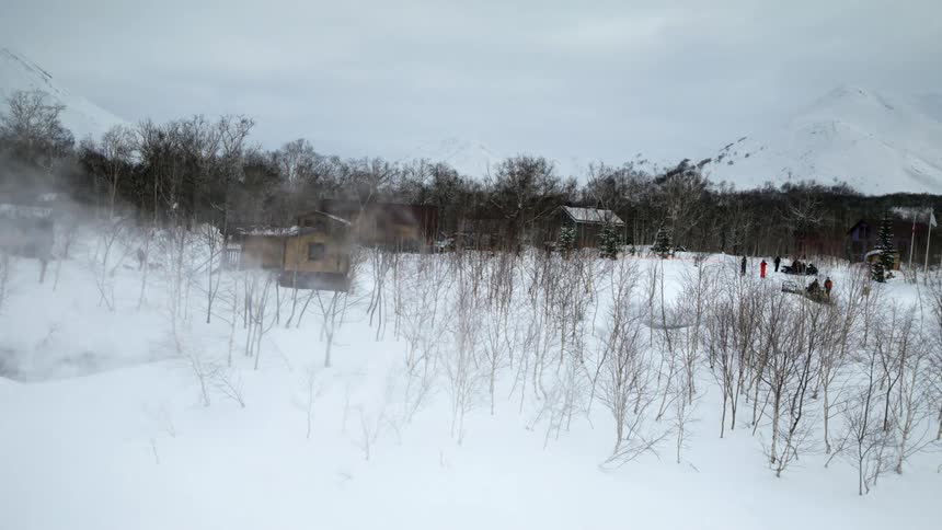 A snowy landscape with bare trees and wooden cabins rising steam or mist from small pools nearby