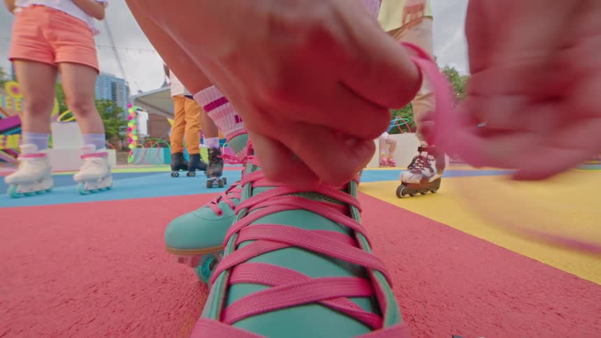 Closeup view of hands tying teal roller skate laces with pink wheels and laces