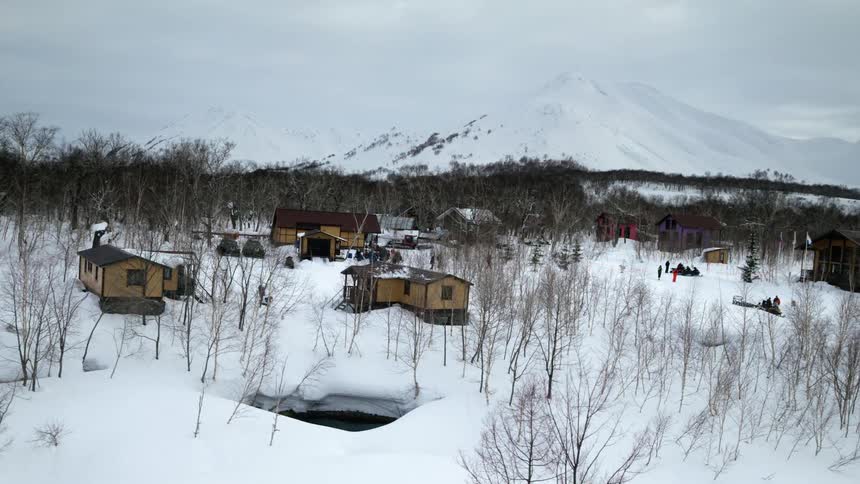 Aerial panorama of small wooden houses in an environment with vegetation and snowcovered mountains
