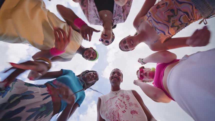 A group of friends dancing in a circle facing downwards toward the camera wearing colorful clothes
