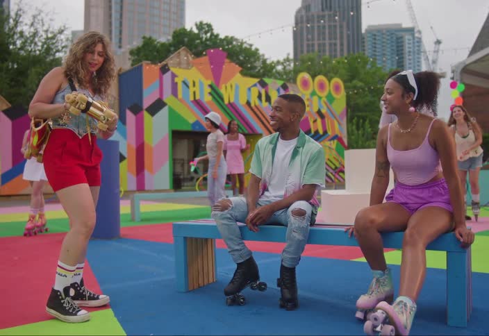 A roller skating scene featuring a group of people enjoying themselves including a woman in red shorts speaking to two seated individuals