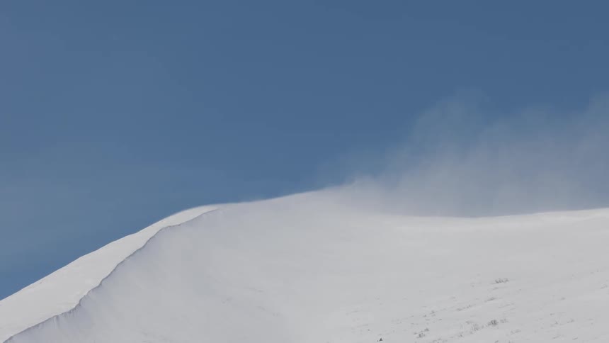 A snowcovered mountain is all white and its top is releasing a little steam into the blue sky