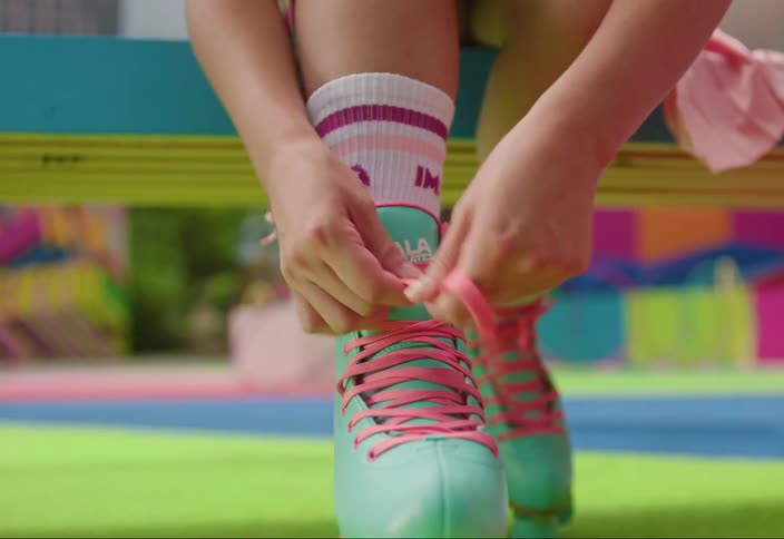 Closeup of hands tying teal roller skate laces with green wheels