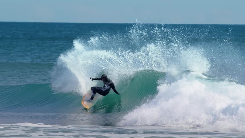 Surfer performs a maneuver on a wave with the sea blue