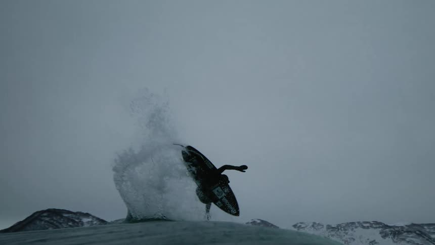 Water sprays as surfer flips in midair on a winter day