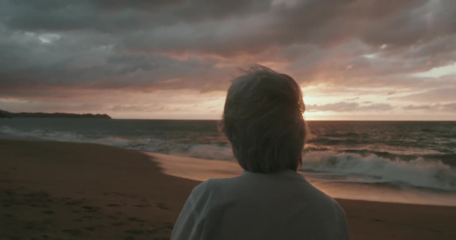 View of a lady from behind enjoying an ocean from a beach on a cloudy sunrise