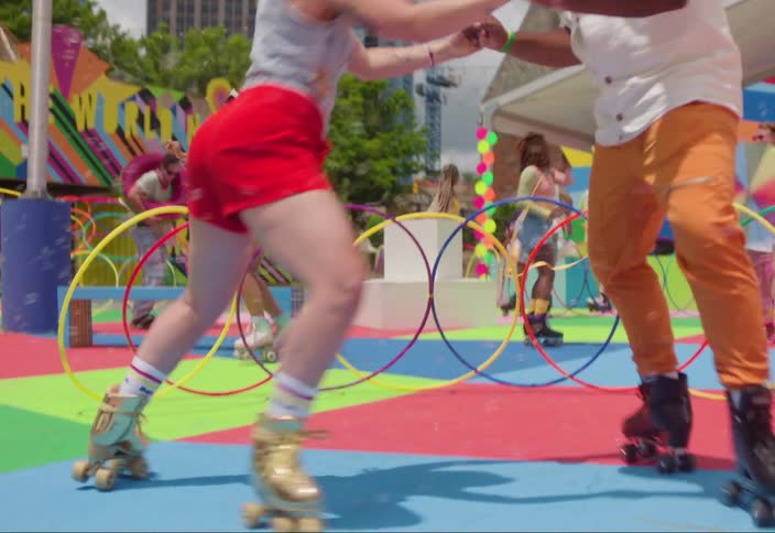 Man and woman holding hands spinning with roller skates and a colorful playground with other people