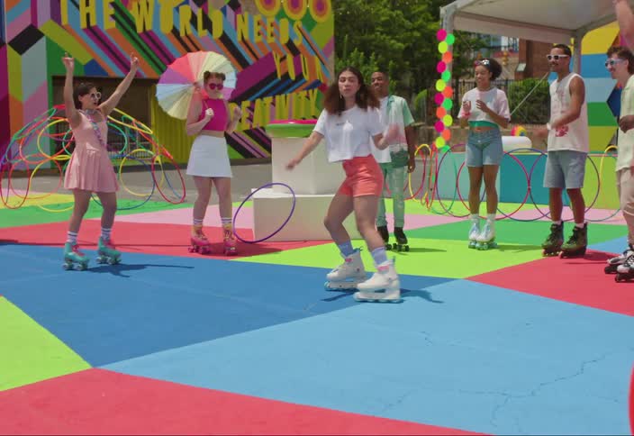A circle of people rollerblading and one of them is spinning and everything around is colorful