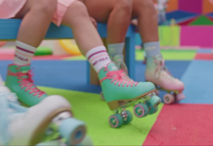Three individuals sit on a blue bench legs crossed wearing colorful roller skates