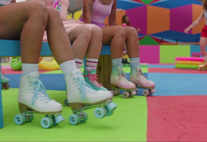 Three women sitting on a bench in a playground showing off their colorful skates