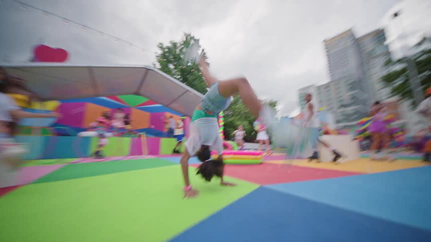 Group of people on a colorful playground rollerblading and a woman doing a backflip