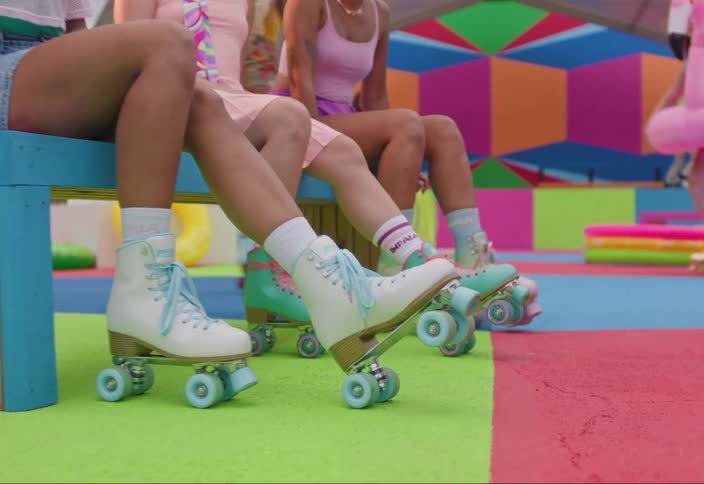 Three young women in colorful roller skating attire sitting on a striped bench at a outdoor skate party