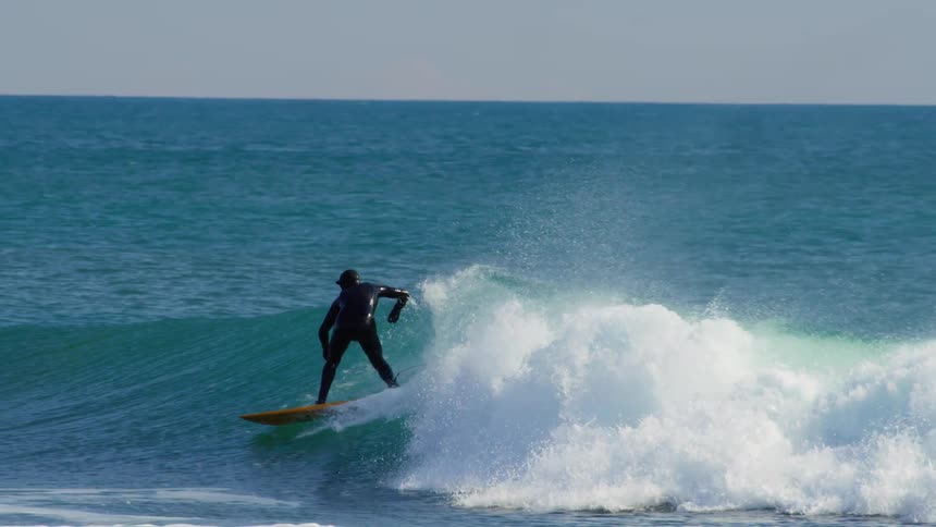 A surfer wearing a full body black wet suit rides a greenishblue wave on a clear day