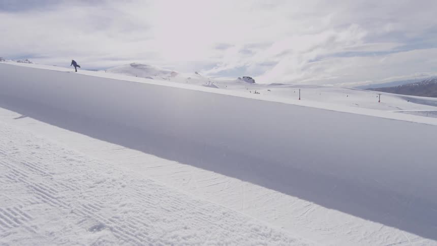 Snowboarder rides across a halfpipe while another walks up the slope