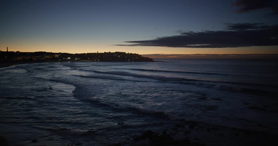 Coastal scene at twilight with the orange and blue sky reflecting on the waters surface and buildings silhouetted on the shore