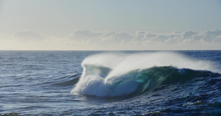 Large wave flowing across the ocean on a cloudy day breaks