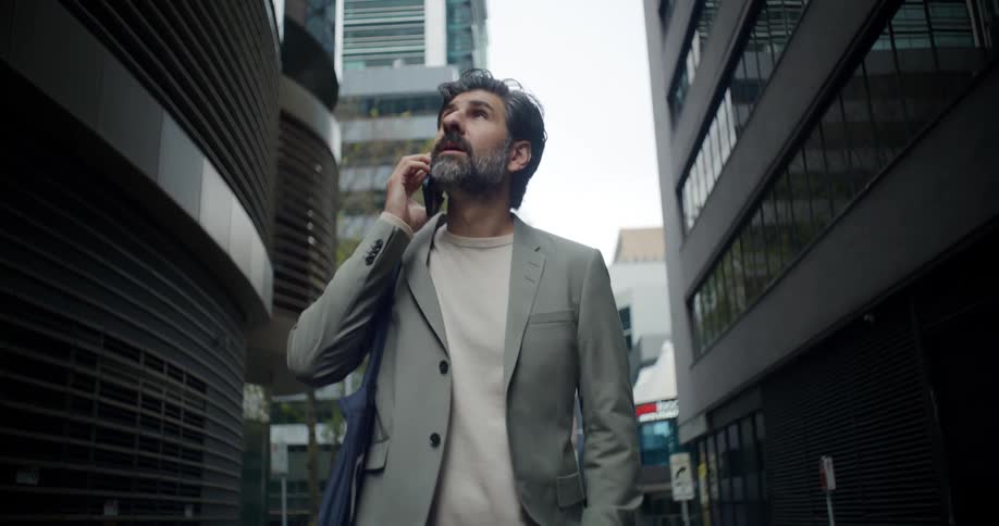 Man walking between downtown skyscrapers answers his smartphone while he looks around