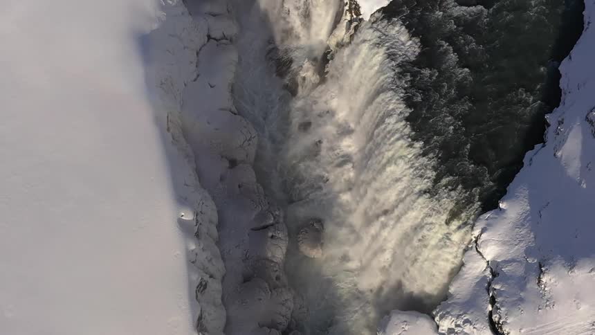 Aerial view of a large waterfall surrounded by snowcapped cliffs