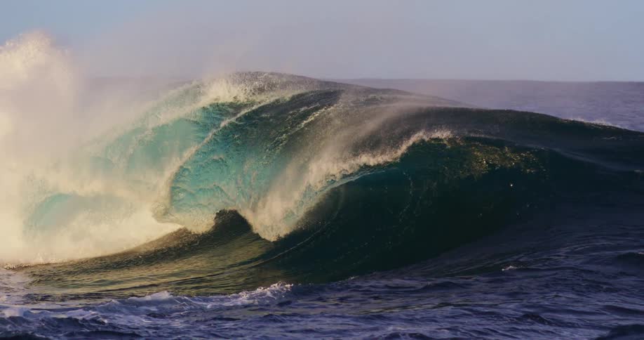 Powerful wave breaks in the ocean with sunlight filtering through the crest