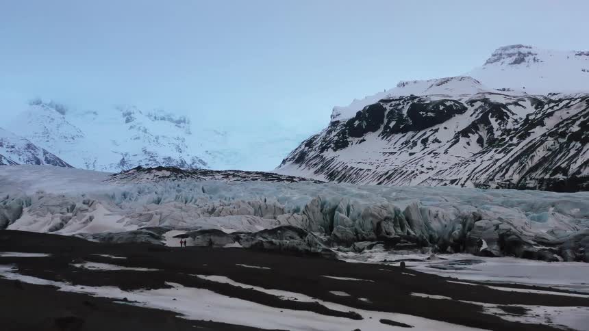 Two people are standing by the ice caps near the mountain