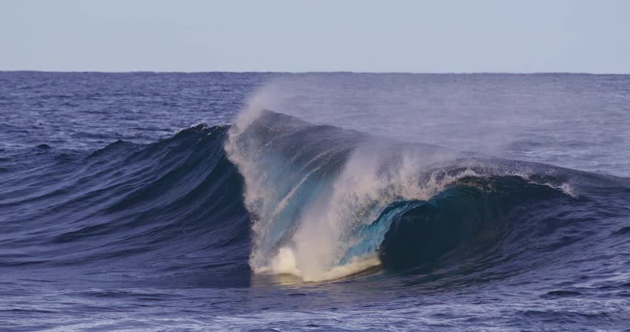 Large wave in the ocean begins to break sending spray into the air