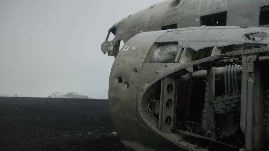 Scrapped airplane sits on black soiled plain with mountains in the distance