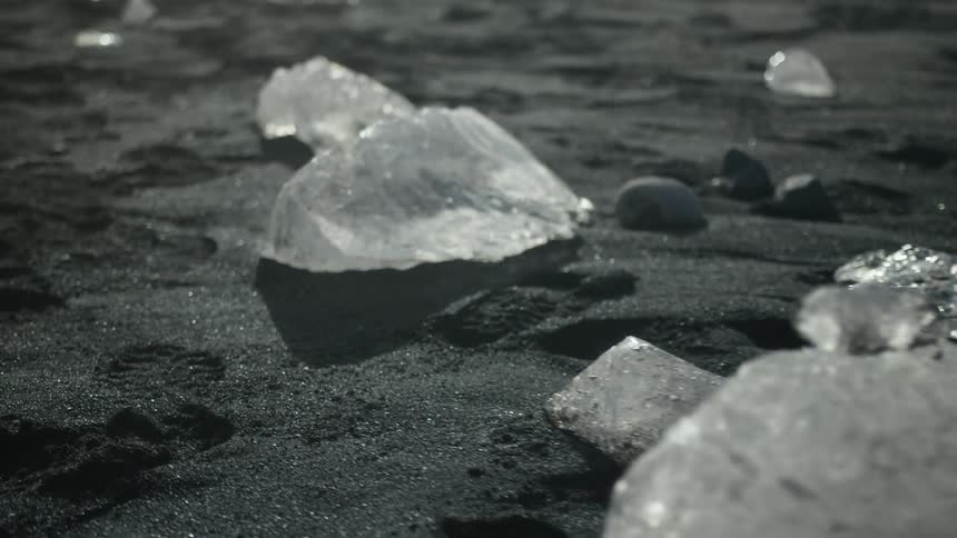 Irregular blocks of ice cast shadows on the dark sand