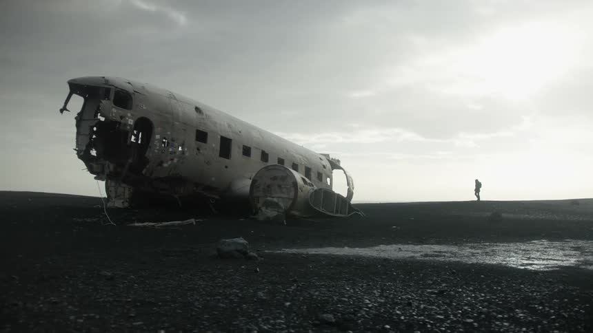 Desolate landscape with the fuselage of a plane lying on the ground and a lonely person in the distance