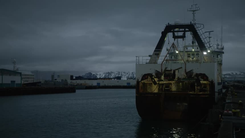 Industrial ship docked in a port with buildings in the background and mountains