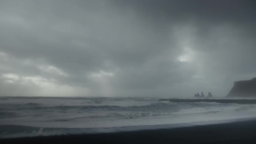 Waves wash ashore on a beach near a cliff and islands