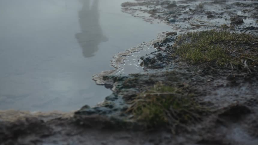 A close up view of a misty landscape featuring a waters edge with the reflection of a person in the water