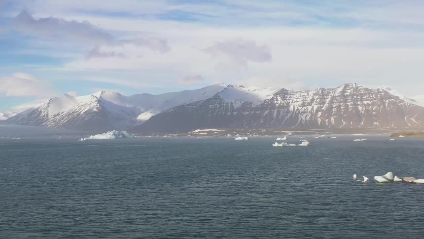 Serene landscape with floating icebergs and a mountain range in the background under a partly cloudy sky