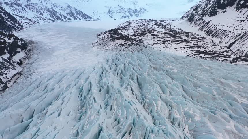 A large glacier fills a large valley ringed by large mountains