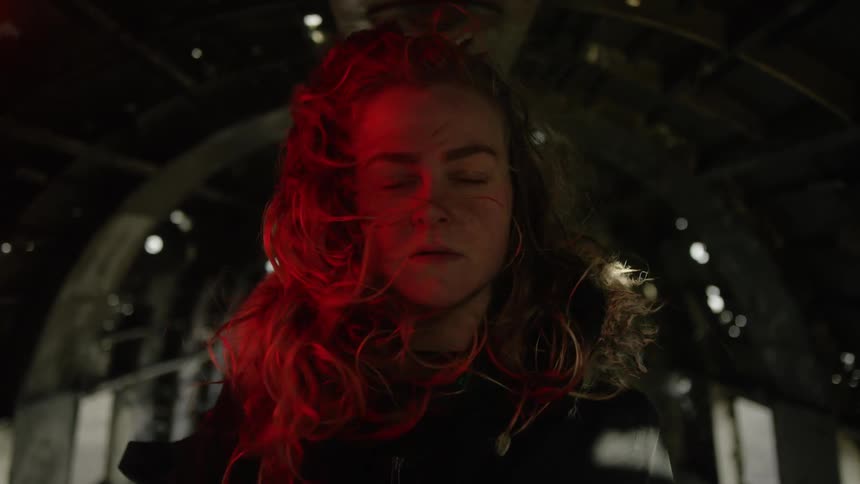 A woman stands in a metal tunnel while the wind blows her long hair around